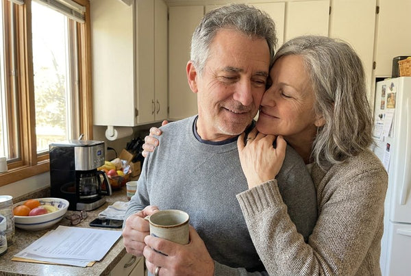 A man hugged warmly by his wife in their kitchen