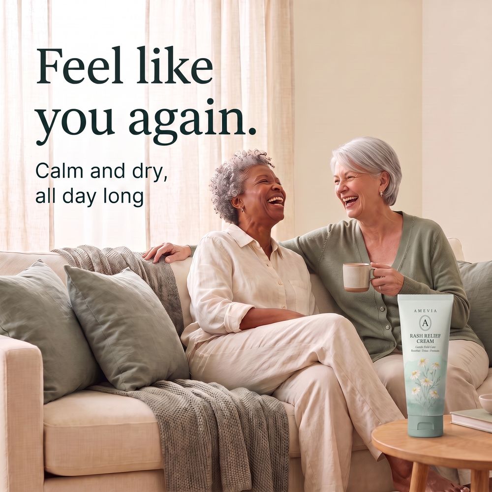 Two women in their sixties laughing together on the sofa, the green Amevia tube on a side table.