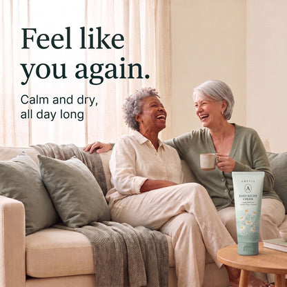 Two women in their sixties laughing together on the sofa, the green Amevia tube on a side table.